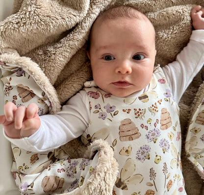 Baby in a bee and floral outfit lying on a soft textured blanket