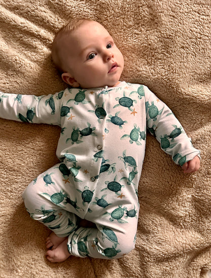 Baby wearing a onesie with turtle pattern lying on a beige blanket