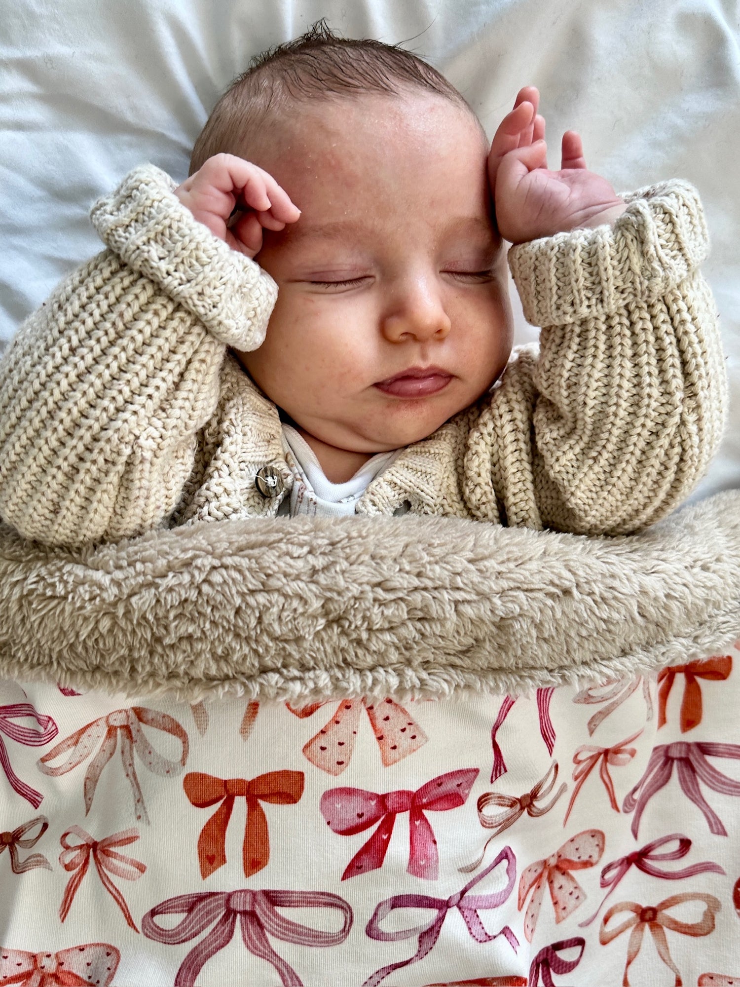 Newborn baby sleeping under a fleece blanket with bow pattern