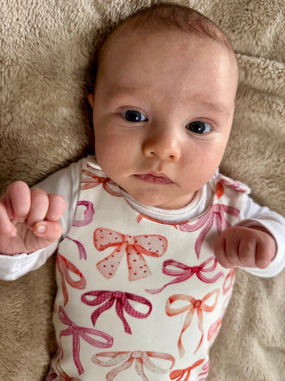 Baby wearing a romper with pink and red bow pattern