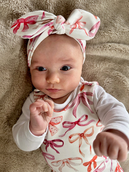 Baby wearing a romper with a pink and red bow pattern with matching head band